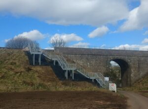 Photo shows and embankment staircase leading from a country road up to railway tracks. There are six landings to accommodate the the topography at the site at Stonehaven.